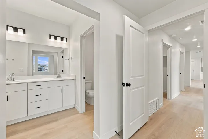 Bathroom featuring a dual-sink vanity with white cabinetry, matte black hardware, a wide wall-to-wall mirror, and wood-finish flooring