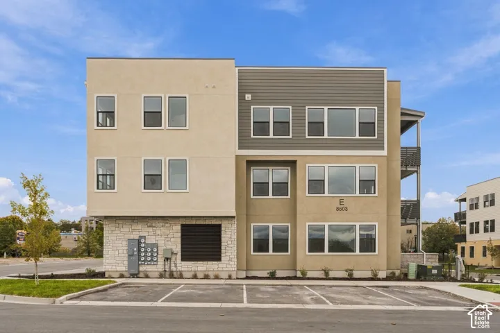 Modern multi-story exterior featuring a mix of stucco and horizontal siding, stone veneer accents, grid-patterned windows, and dedicated off-street parking