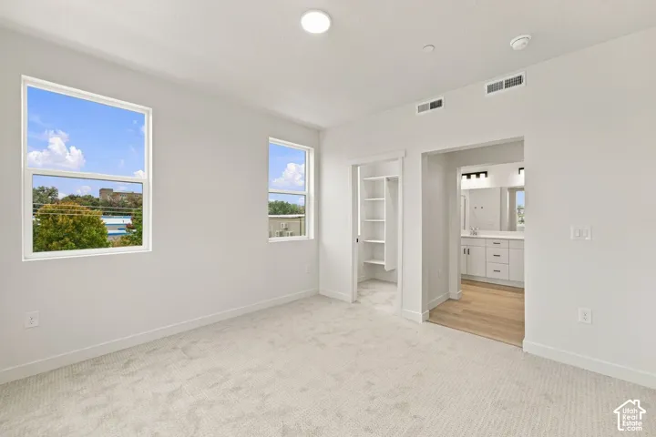 Neutral interior featuring neutral carpeting, recessed ceiling lighting, dual windows, walk-in closet with built-in shelving, and wood-finish flooring