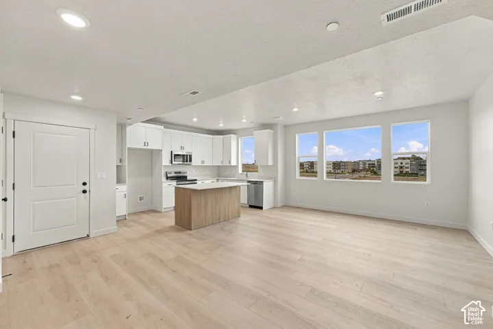 Kitchen featuring white cabinetry, an island with wood-finish base, stainless steel appliances, recessed lighting, and wood-finish flooring