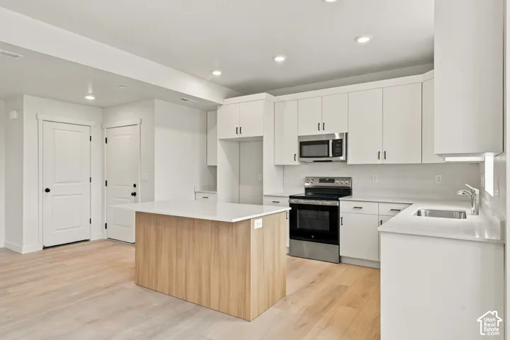 Kitchen featuring white shaker-style cabinetry, a central island with wood-finish paneling, white quartz countertops, stainless steel appliances, and wood-finish flooring