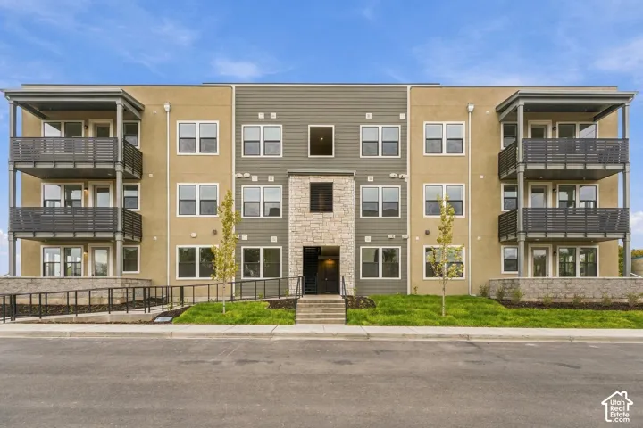 Multi-story exterior featuring a mix of stucco and horizontal siding, stacked balconies with metal railings, and a natural stone-veneer entry facade