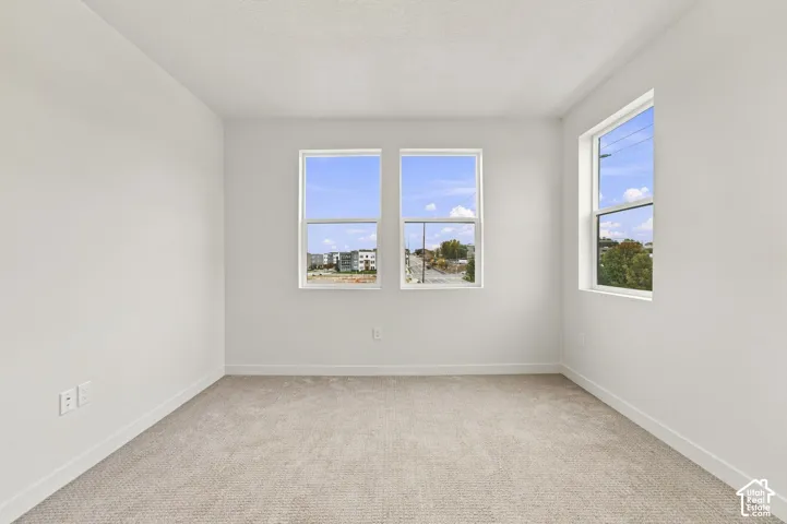 Neutral-toned carpeted flooring, white wall finishes, and triple windows providing natural light