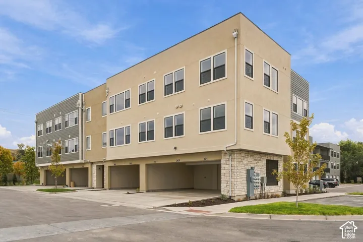 Multi-level exterior featuring tan stucco and grey horizontal siding, stone veneer accents, and covered ground-level parking