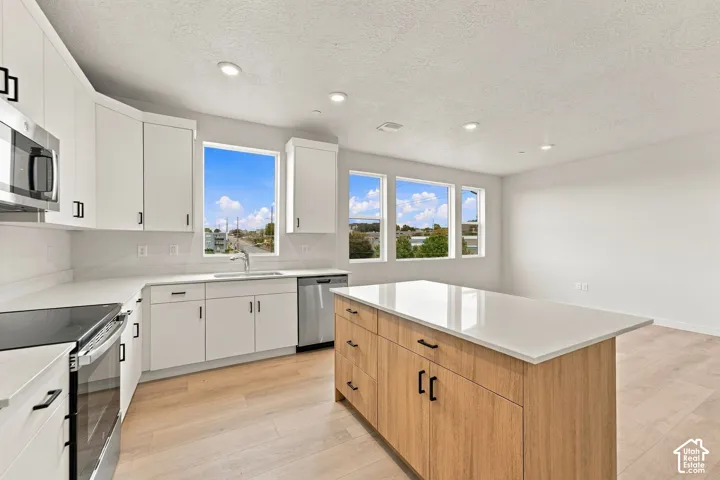 Kitchen featuring white cabinetry, light-toned countertops, a wood-finish island, stainless steel appliances, and large windows