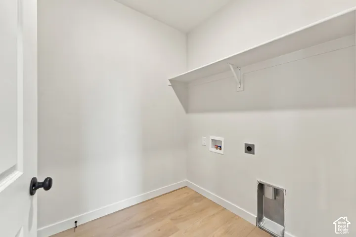 Utility space featuring wood-finish flooring, a wall-mounted shelving unit, and dedicated hookups for laundry appliances
