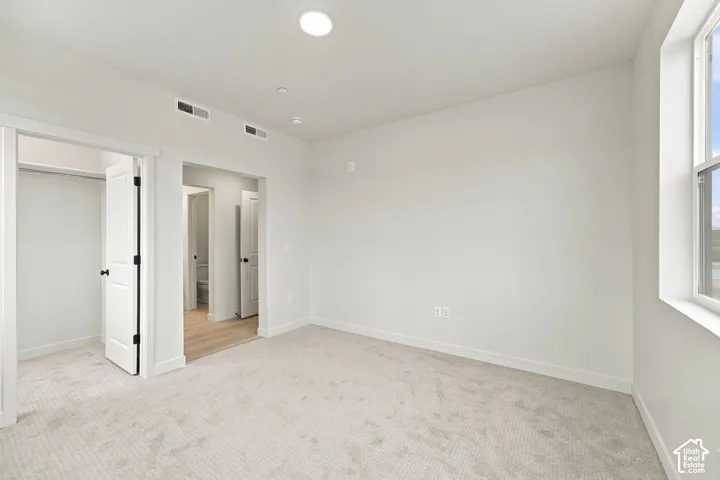 Interior room featuring neutral wall-to-wall carpeting, recessed ceiling lighting, a large window with natural light, and two doorways leading to auxiliary spaces