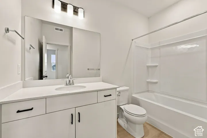 Bathroom featuring a vanity with a white countertop, undermount sink, matte black hardware, integrated tub and shower surround, and three-light wall fixture