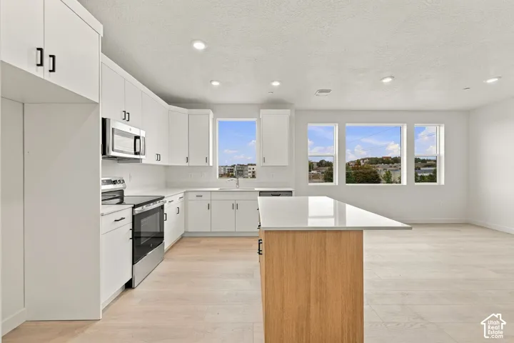 Kitchen featuring white shaker cabinetry, quartz countertops, a central island with wood-finish base, stainless steel appliances, and wood-finish flooring