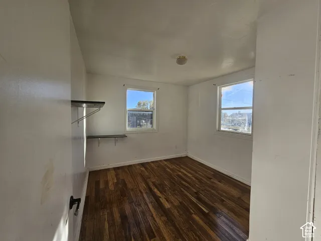 Room featuring wood-finish flooring, two windows with natural light, and two wall-mounted storage shelves