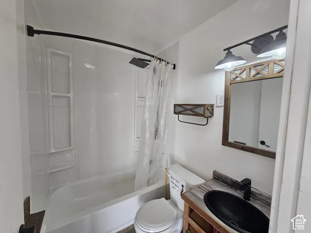 Bathroom featuring a white tub-shower combination, vanity with a patterned surface, integrated black vessel sink, dark finish faucet, and farmhouse-style wall-mounted light fixture