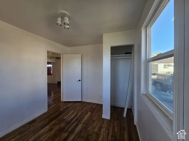 Room featuring wood-finish flooring, a multi-bulb flush mount ceiling light fixture, a closet with a built-in rod and shelf, and a large window