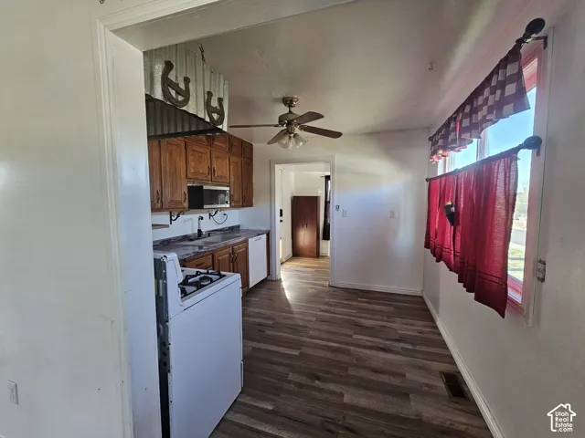 Kitchen featuring wood cabinetry, wood-finish flooring, a white gas range, a built-in microwave, and a ceiling fan