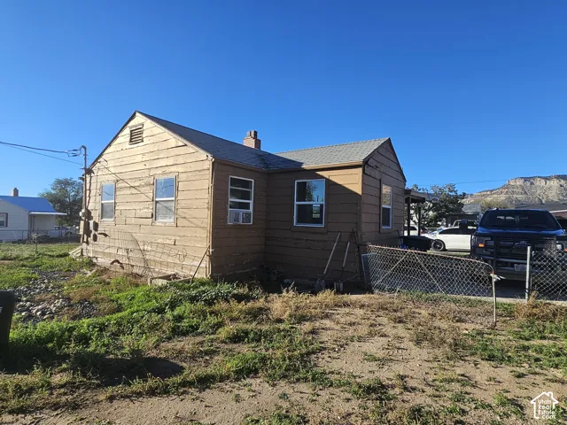 Single-story residence featuring horizontal lap siding, a pitched roofline, a masonry chimney, and a chain-link fenced perimeter