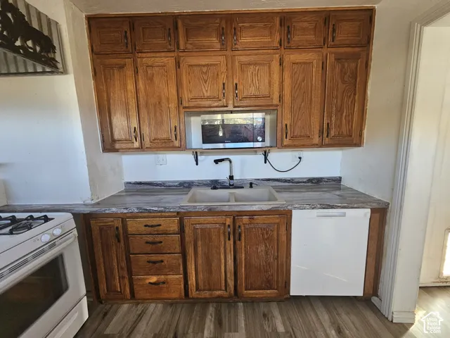 Kitchen featuring wood cabinetry, integrated microwave, dual-basin sink with high-arc faucet, and wood-finish flooring