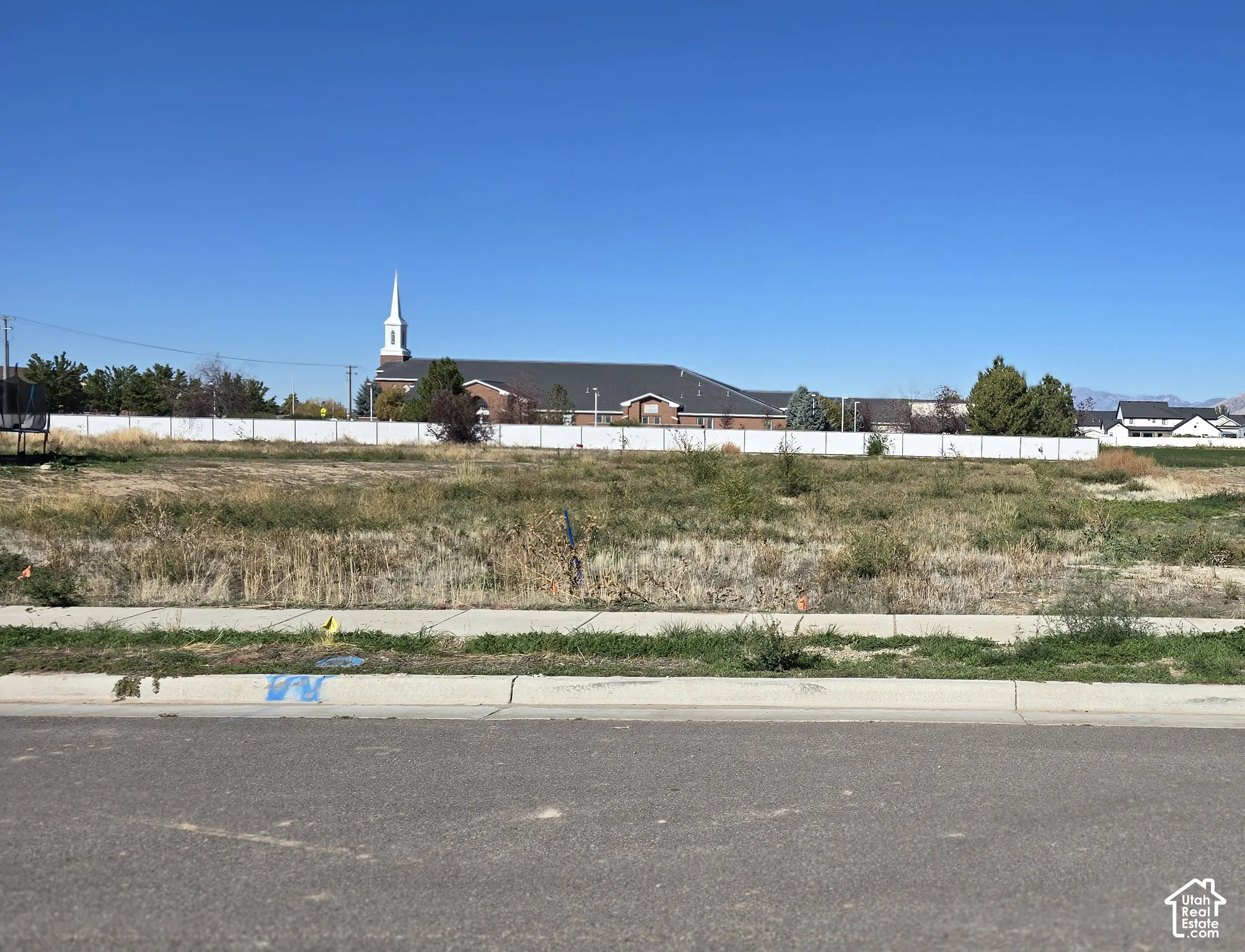 Cleared residential lot featuring paved street access, concrete curbing, and a white perimeter fence