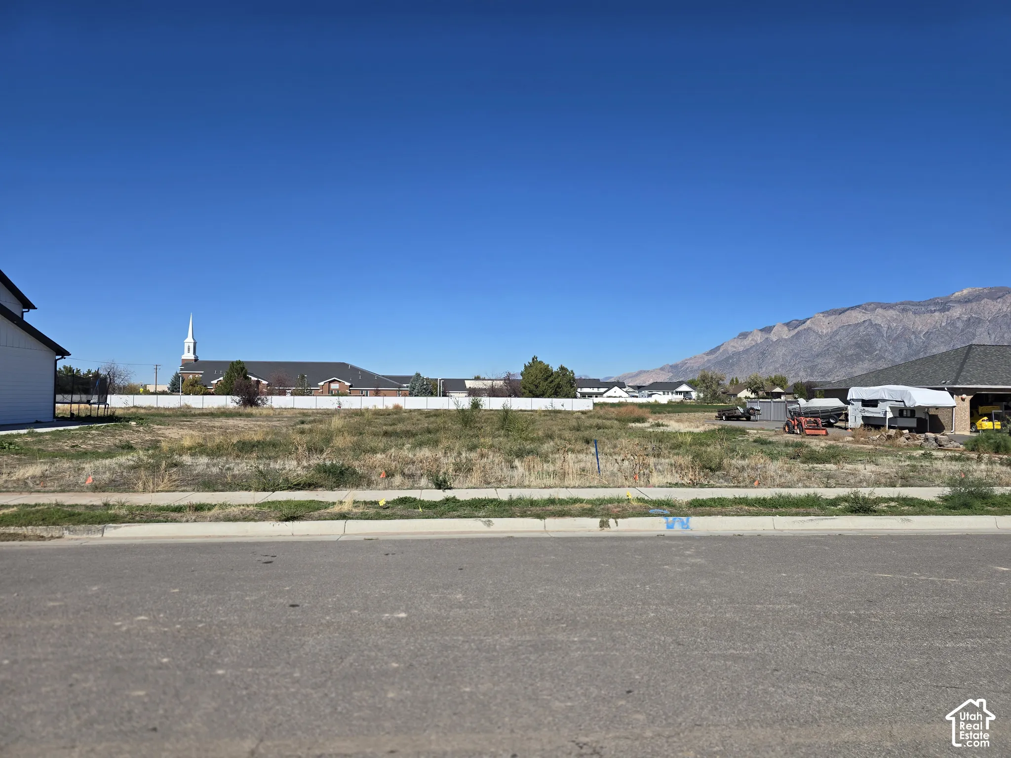 Cleared residential lot featuring paved street access, concrete curbing, and mountain scenery