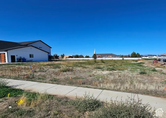 Expansive level lot featuring a concrete sidewalk and white perimeter fencing