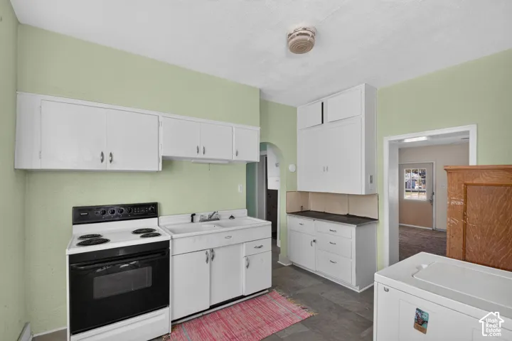 Kitchen featuring white cabinetry with extended-height uppers, double-basin sink, electric range, and stone-finish tile flooring
