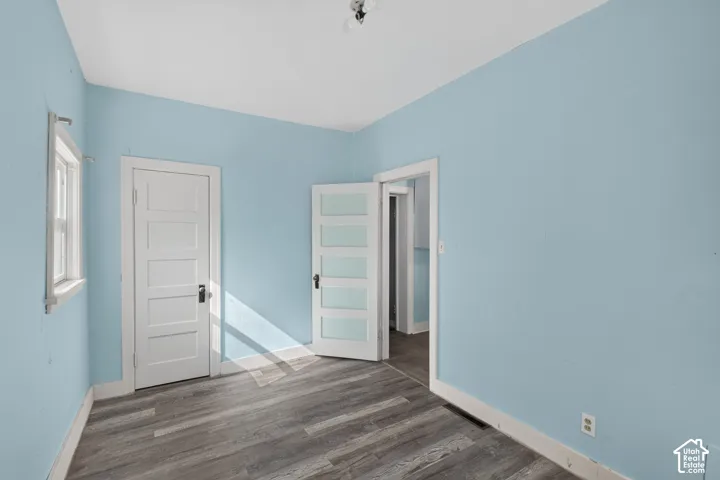 Room featuring wood-finish flooring, a white five-panel interior door, a white door with glass panes, and a window with white trim