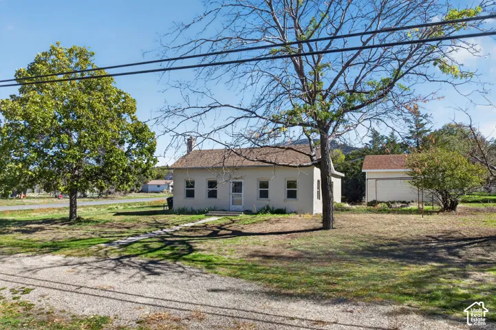 Single-story residence featuring a light-colored stucco exterior, asphalt shingle roof, chimney, and mature trees on a level lot