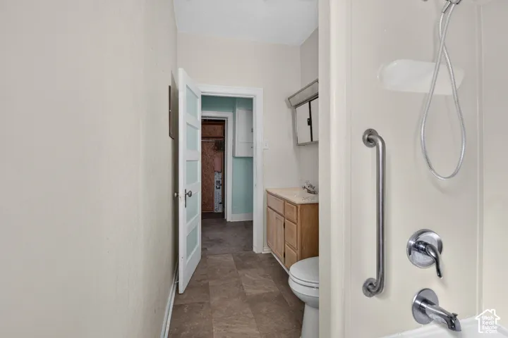 Bathroom featuring a shower unit with an integrated grab bar, wood-finish cabinetry, tile-style flooring, and a multi-panel door with frosted glass inserts