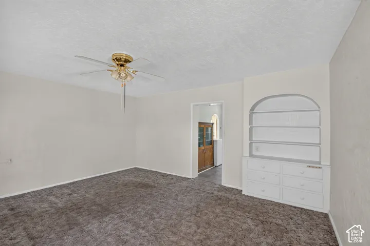 Room featuring carpeting, a centrally mounted ceiling fan with integrated lighting, and a built-in arched storage unit with lower cabinetry and shelving