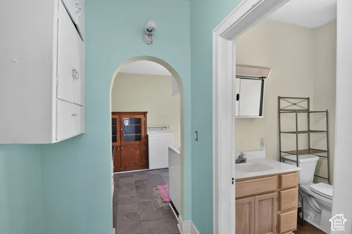 Arched doorway featuring white built-in cabinetry, stone-finish tile flooring, a wood-finish vanity with a white countertop, and a surface-mounted medicine cabinet
