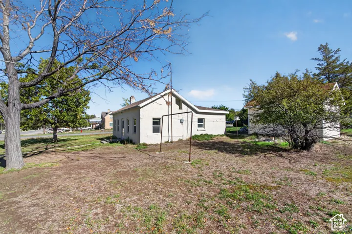 Stucco exterior featuring a gabled roofline, multiple windows, and detached outbuilding situated on an expansive lot with mature trees