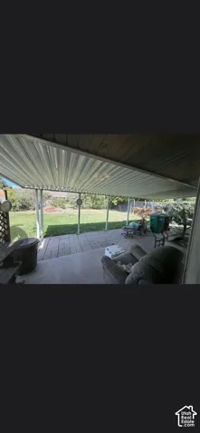 Covered patio featuring a corrugated metal roof and concrete paver flooring, opening to a fenced backyard with a grass lawn