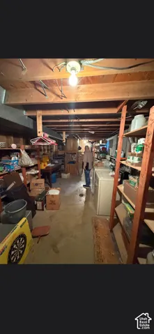 Unfinished basement storage area featuring exposed wood joists, concrete flooring, and built-in wooden shelving units