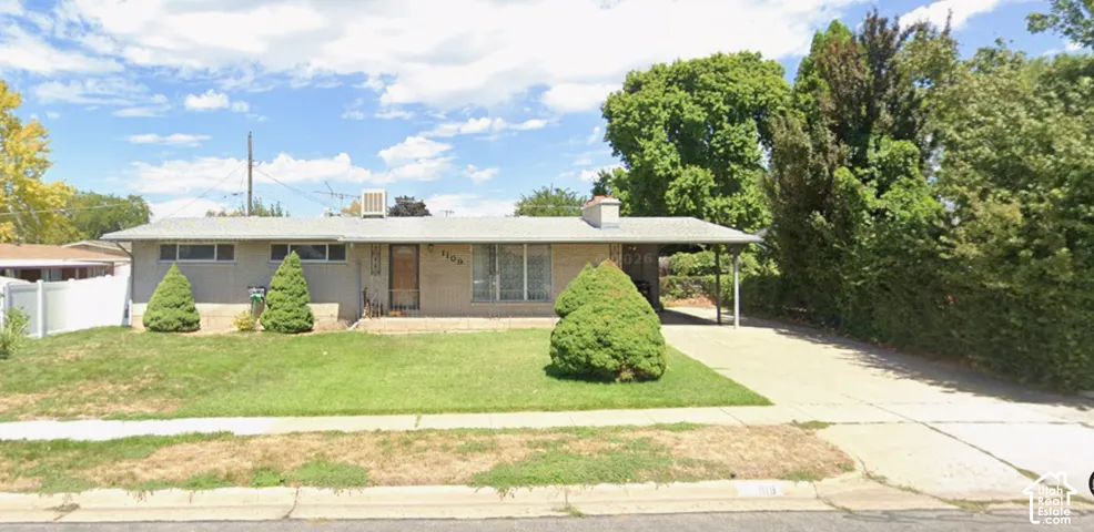 Single-story residence featuring a brick facade, covered carport, concrete driveway, and front lawn with mature landscaping