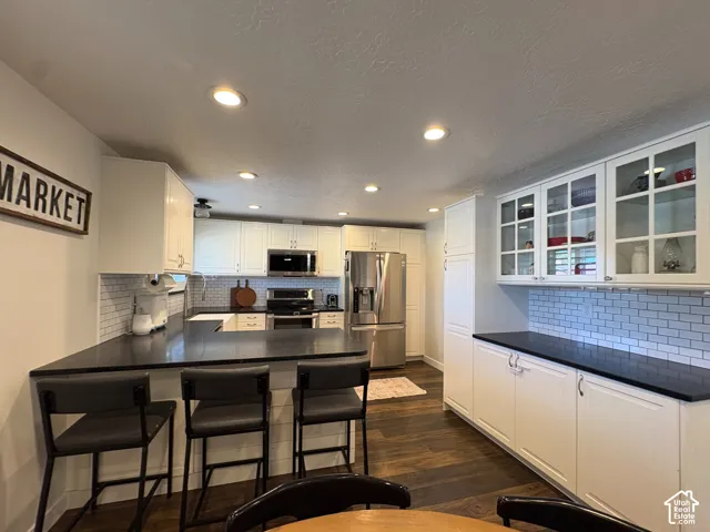 Kitchen featuring white cabinetry, black countertops, subway tile backsplash, stainless steel appliances, and recessed lighting
