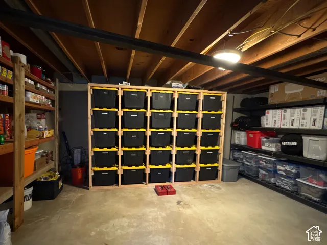 Storage area featuring exposed timber ceiling joists, concrete flooring, and built-in wood shelving units