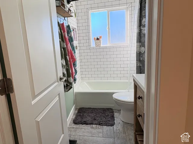 Bathroom featuring white subway tile wall surround, wood-finish flooring, a porcelain tub-shower combination, and a vanity with a white countertop