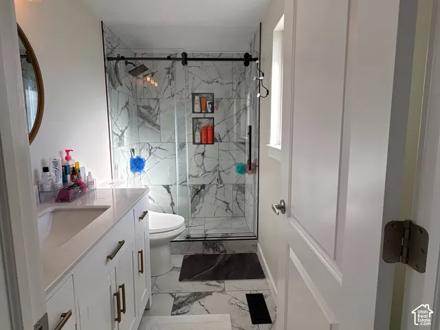 White vanity cabinet with a light-toned countertop, shower enclosure with black hardware, and large-format tile flooring