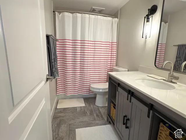 Bathroom featuring herringbone-patterned tile flooring, gray vanity with sliding cabinet doors, solid-surface countertop with integrated basin, and black metal light fixtures