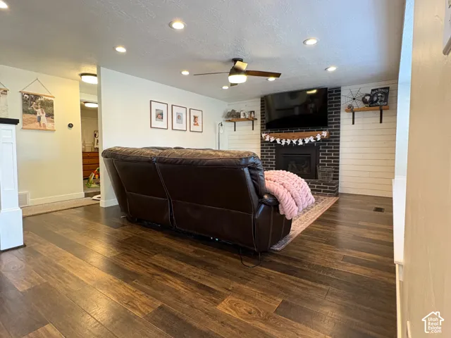 Living area featuring wood-finish flooring, recessed lighting, ceiling fan, dark brick fireplace, and horizontal slat wall accents