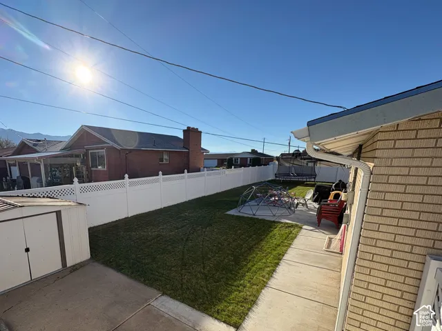 Backyard featuring a manicured lawn, concrete patio, perimeter vinyl fencing, and a detached metal storage structure
