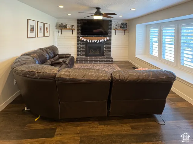 Brick fireplace with a wood mantel, wood-finish flooring, recessed lighting, ceiling fan, and bay window featuring plantation shutters