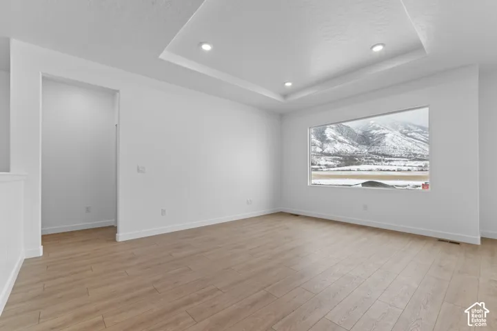 Tray ceiling with recessed lighting, wood-finish flooring, and a large picture window showcasing mountain scenery