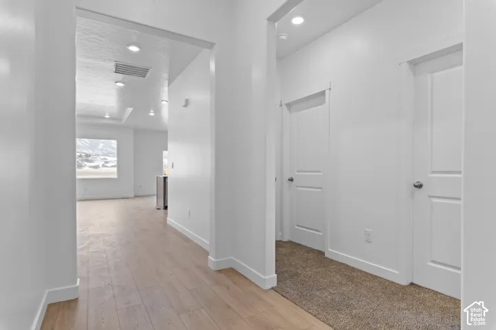 Interior hallway featuring light-toned wood-finish flooring, neutral carpeting, recessed ceiling lighting, and two-panel interior doors