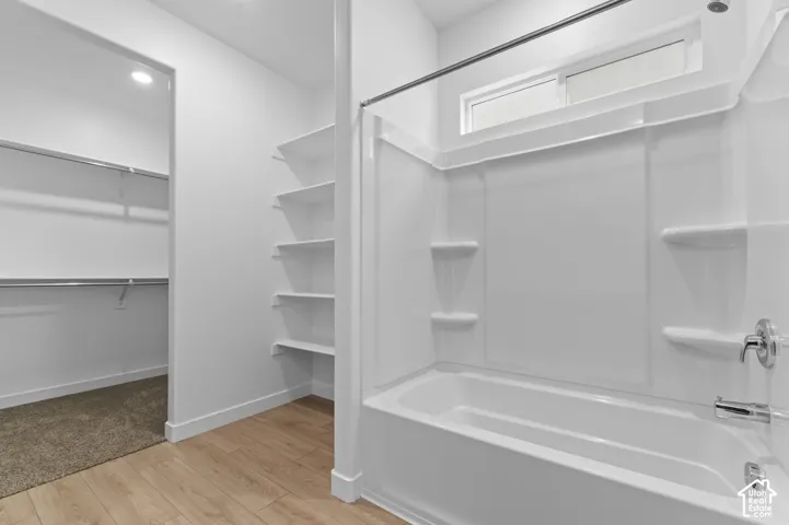 Bathroom featuring a white molded tub surround with integrated shelving, polished chrome fixtures, wood-finish flooring, and built-in wall shelving