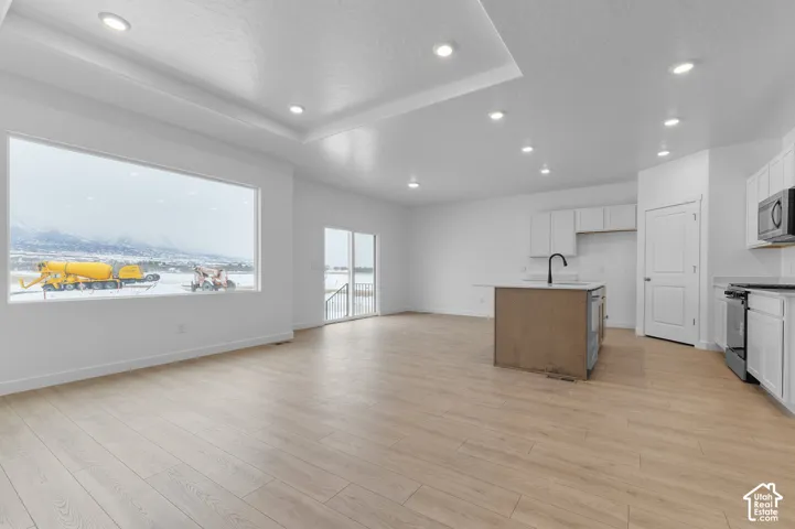 Open-concept interior featuring wood-finish flooring, recessed lighting, tray ceiling, kitchen island with dark finish cabinetry, and a large picture window