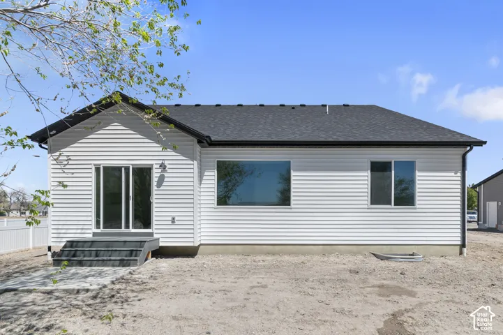 Horizontal siding exterior featuring a dark asphalt shingle roof, sliding glass patio door, concrete step, and window well