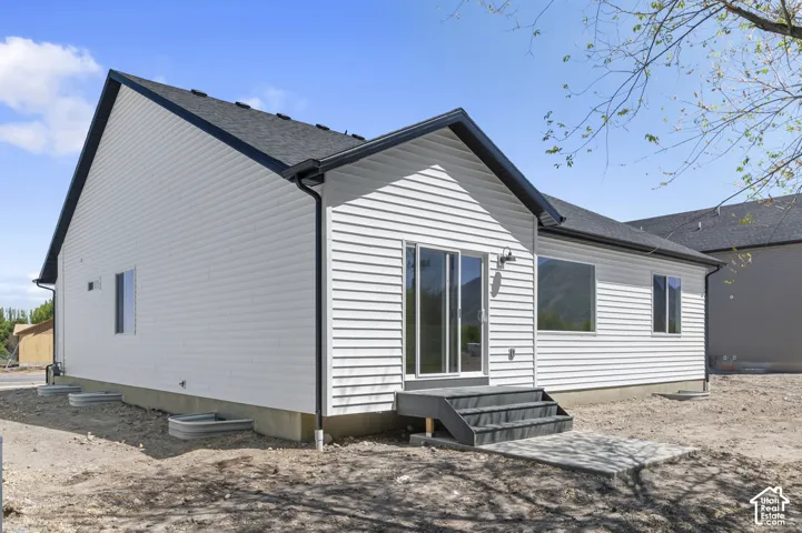 Single-story residence featuring white horizontal siding, a dark-toned gable roof, a concrete patio, and a sliding glass door