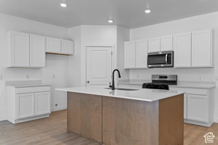 Kitchen featuring white shaker-style cabinetry, wood-finish center island with a stone-composite countertop, stainless steel appliances, and wood-finish flooring
