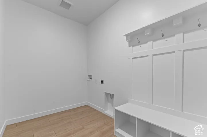 Built-in white mudroom bench with paneled backing and integrated coat hooks, complemented by wood-finish flooring and dedicated laundry utility connections