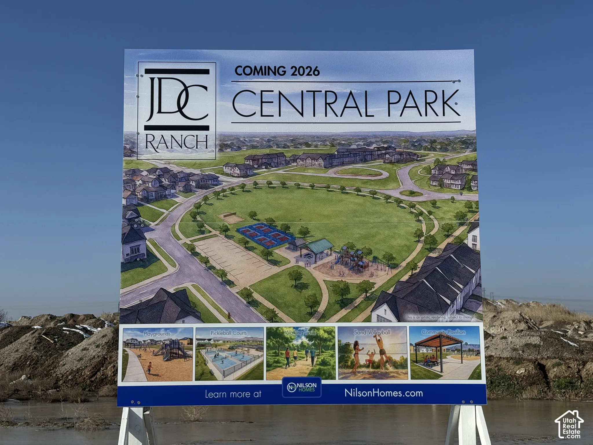 Planned community development featuring a central green space, paved pathways, pickleball courts, playground equipment, and a covered pavilion