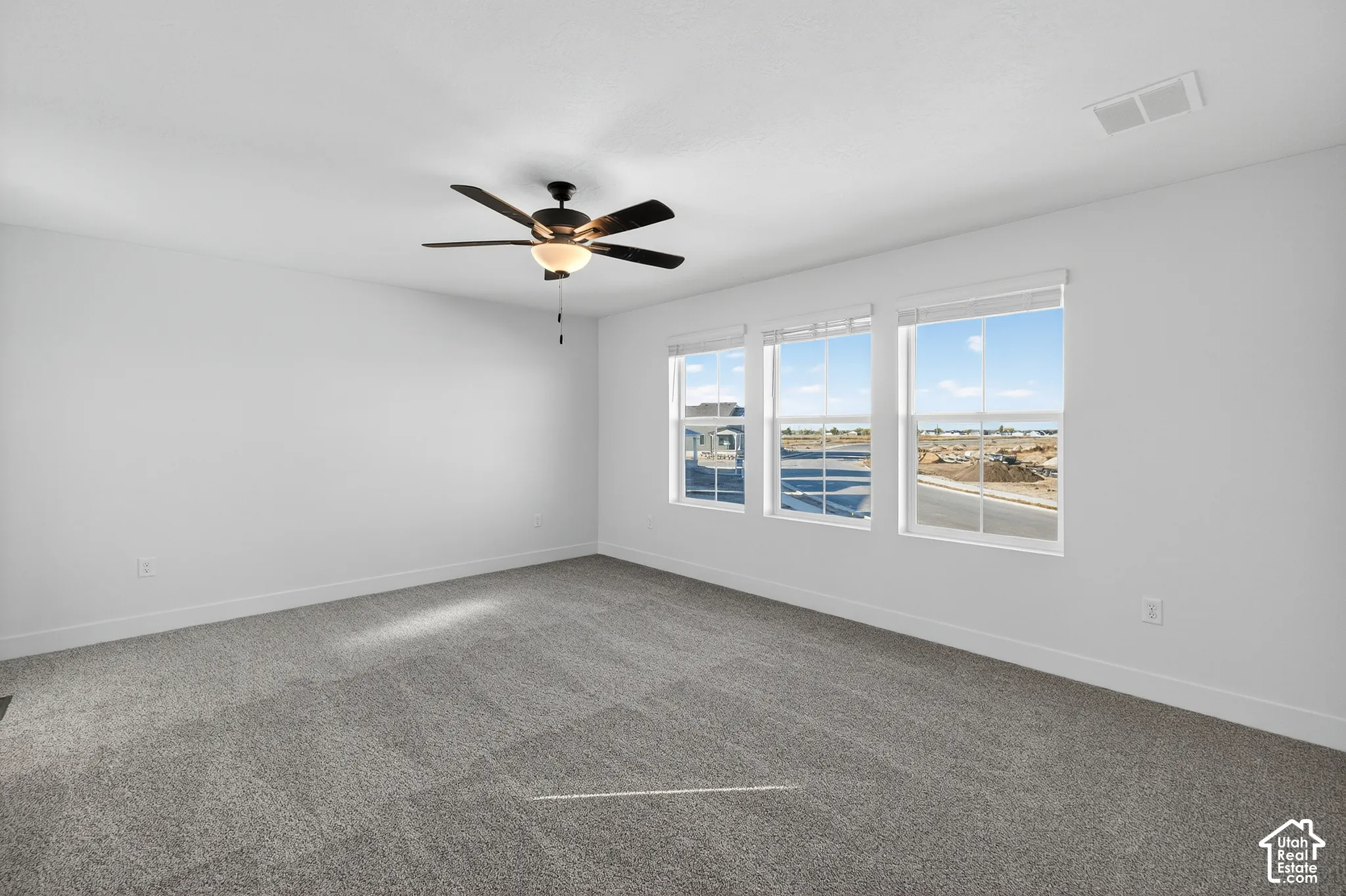 Room featuring neutral wall-to-wall carpeting, three grid-pattern windows, and a multi-blade ceiling fan with integrated light fixture